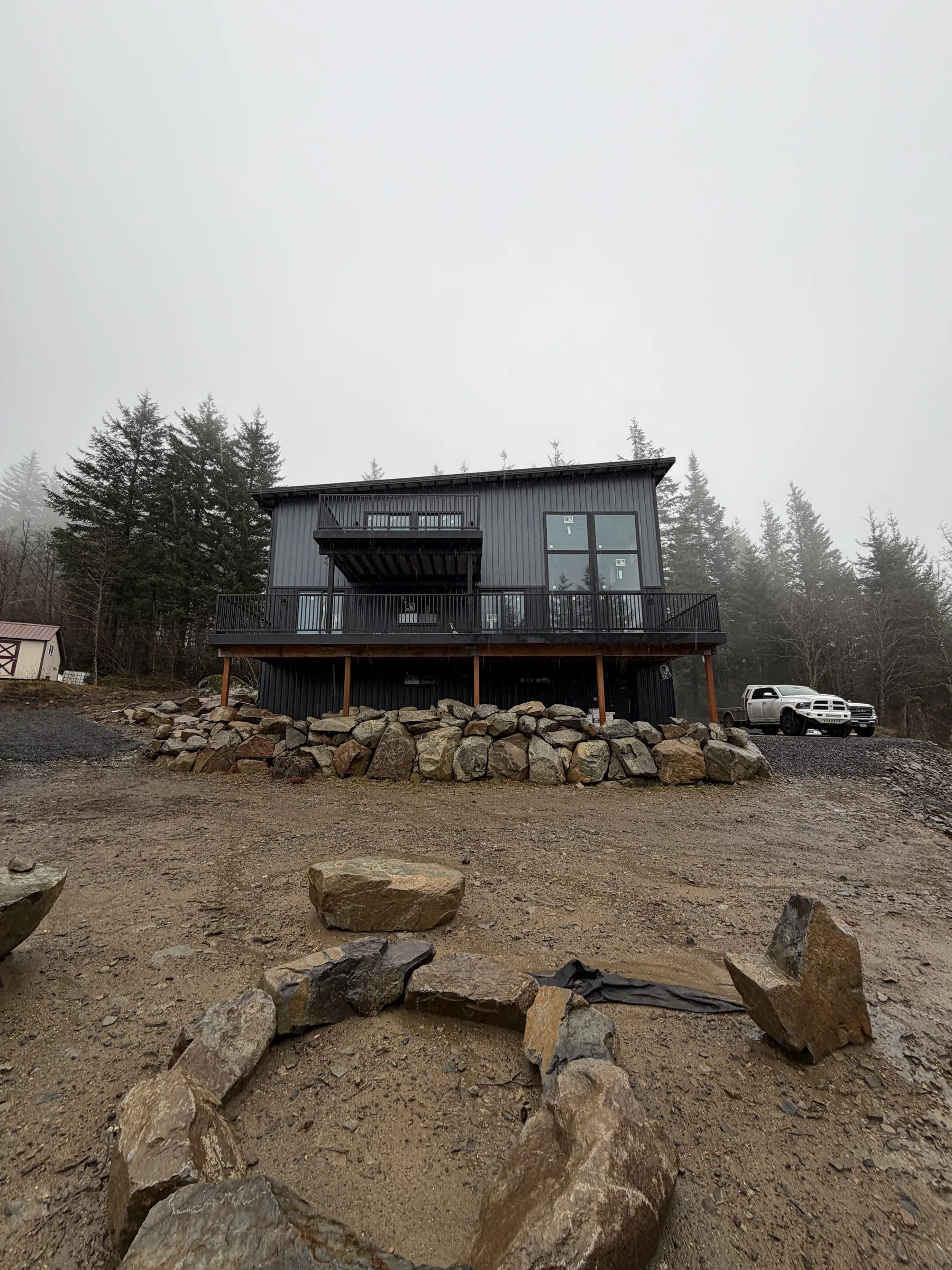 The black house on a rock bench — An ICF shell finished in black, with a wraparound deck, boulder terraces, and a fire pit court