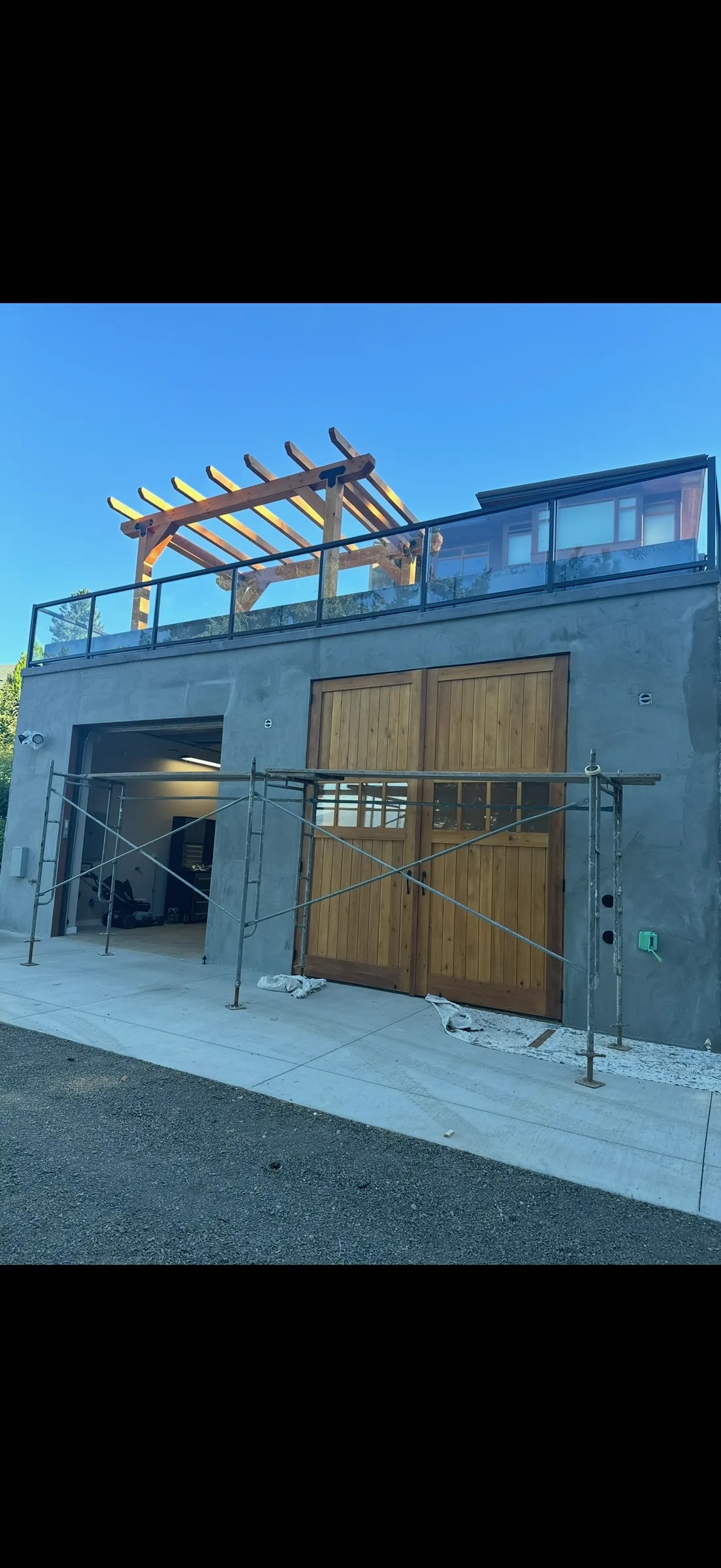 A garage under a rooftop terrace — ICF retaining walls carrying a concrete deck, a glass rail, and a timber pergola overhead